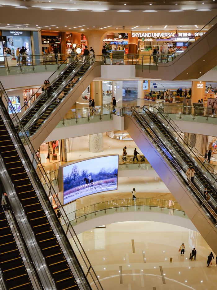 Busy multi-level shopping mall featuring escalators and shoppers.
