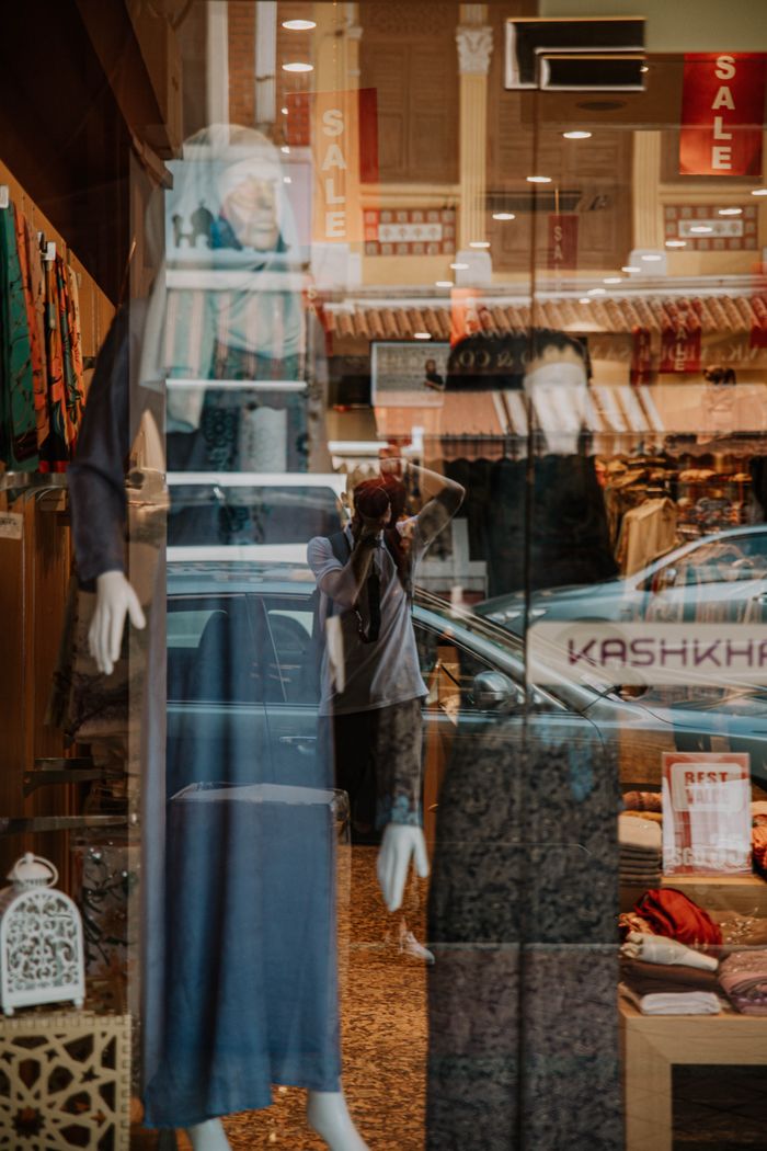 Creative photo of mannequins in a store window with reflections and background details.